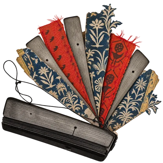 A bound palm-leaf manuscript fanned open into eight leaves of palm leaf, red woven cloth and indigo cut paper, with a loose black cord.